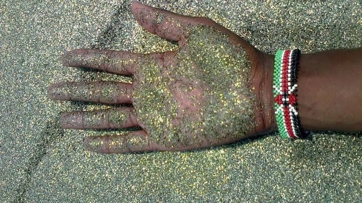 A palm pressed into golden sand, a beaded Kenyan-flag bracelet at the wrist