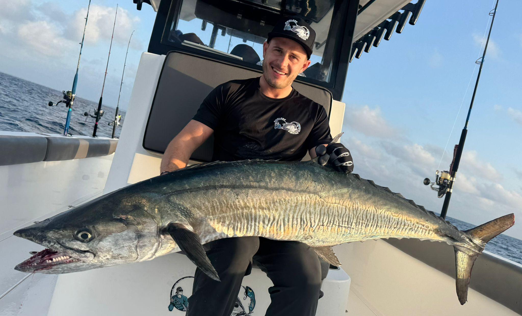 An angler seated on deck holding a long kingfish across his lap