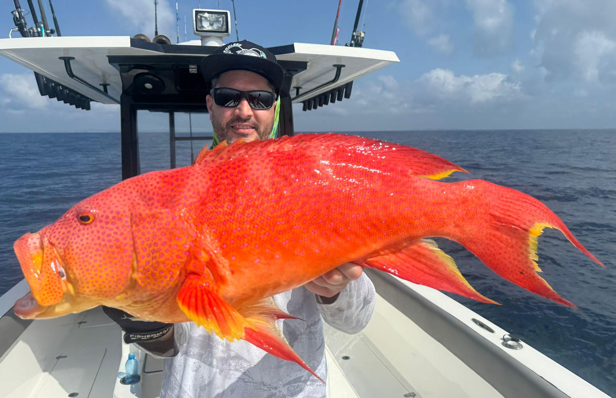 An angler holding up a bright red lyretail grouper at sea