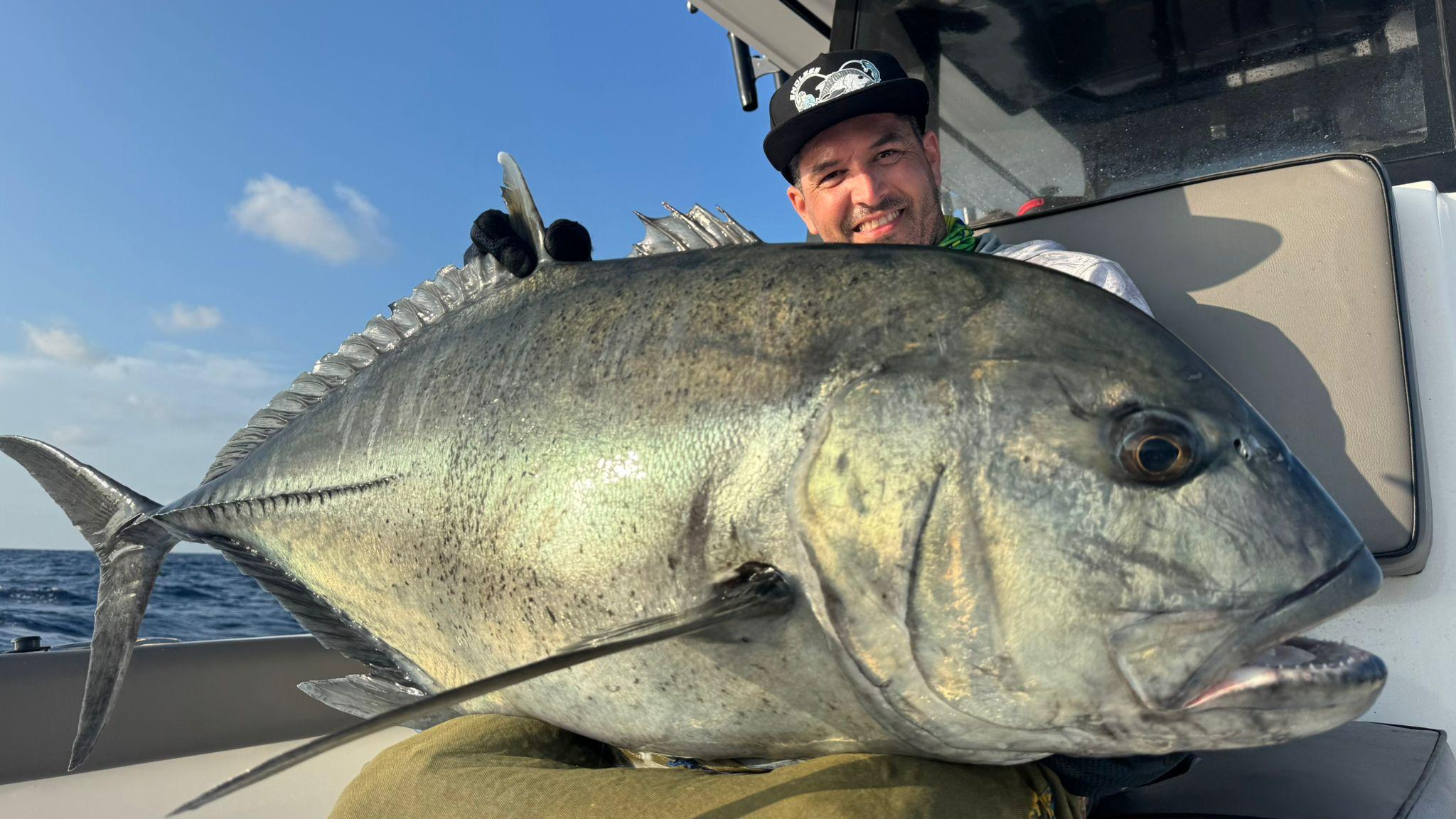 An angler in the cockpit holding a large silver giant trevally