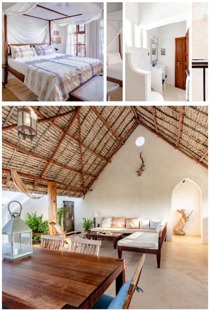 A four-poster bed under a mosquito net, a white bathroom, and a sitting room open to a high makuti roof