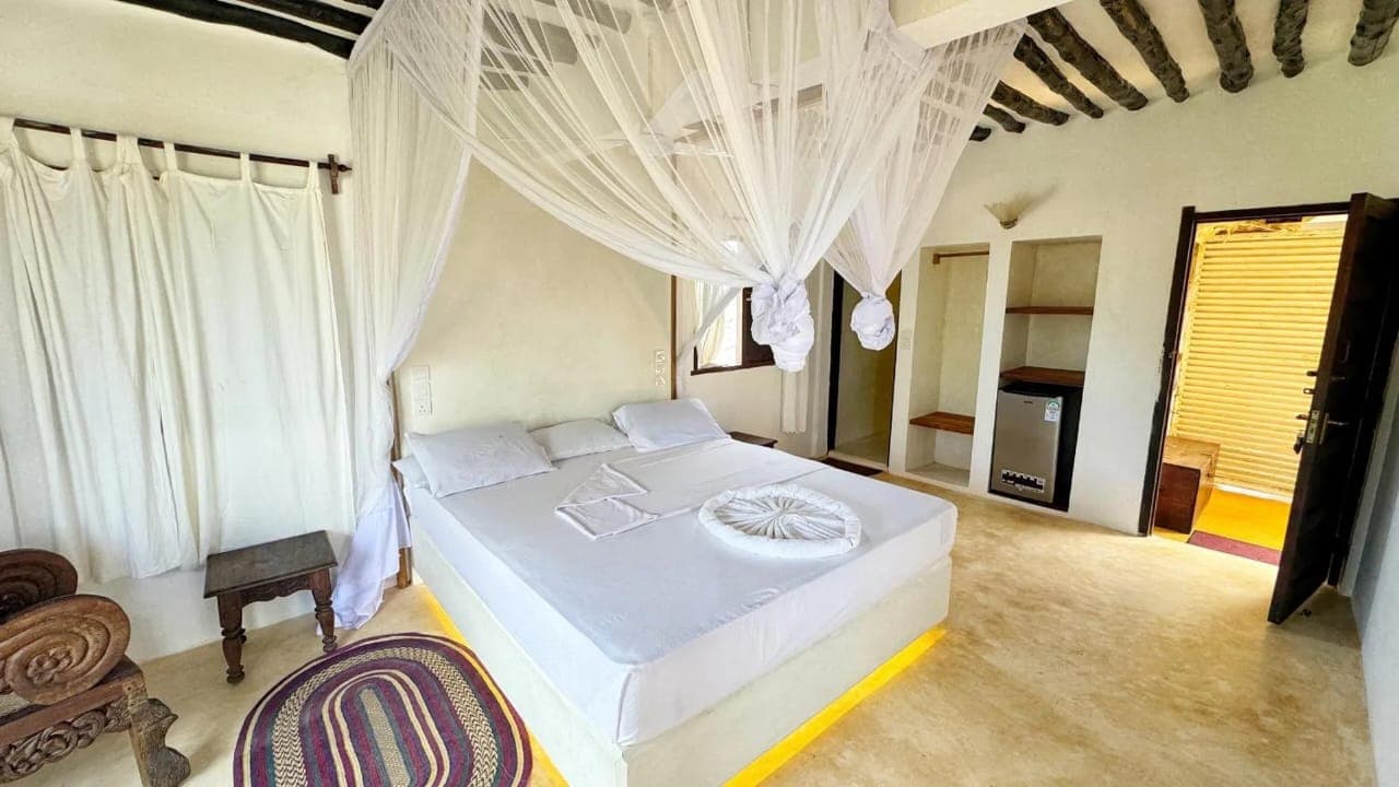 A large bedroom with a bed under a tied mosquito net, a carved chair and a door through to the bathroom