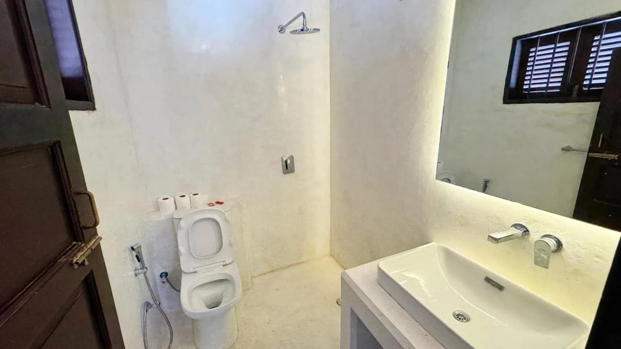 A white plaster shower room with a rain head, basin and backlit mirror
