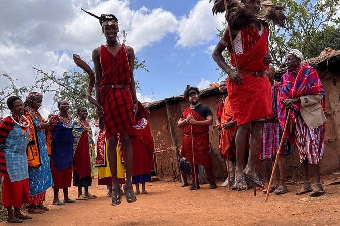 Maasai men performing the adumu jumping dance outside a manyatta while visitors watch