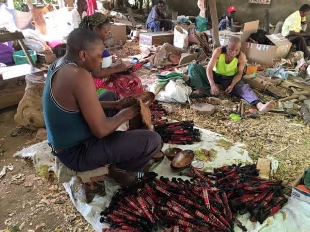 Woodcarvers at work on the ground among piles of carved pieces