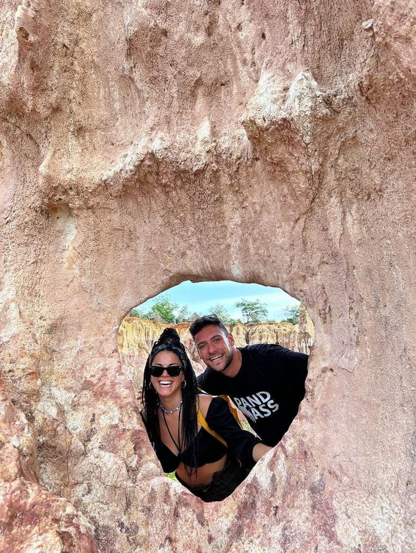 2 visitors smiling through a natural window in the pink sandstone at Marafa