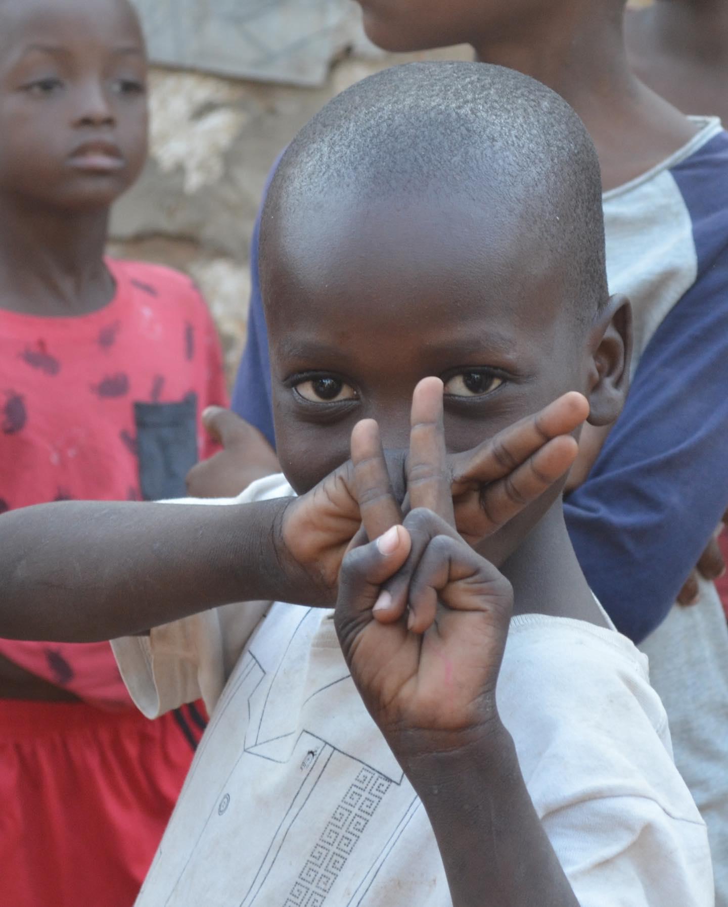 A boy looking straight at the camera with his fingers raised, other children behind him