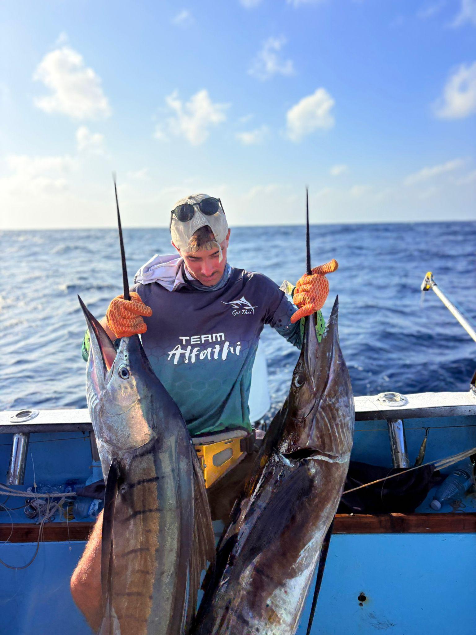 An angler on deck holding up 2 sailfish by the bill