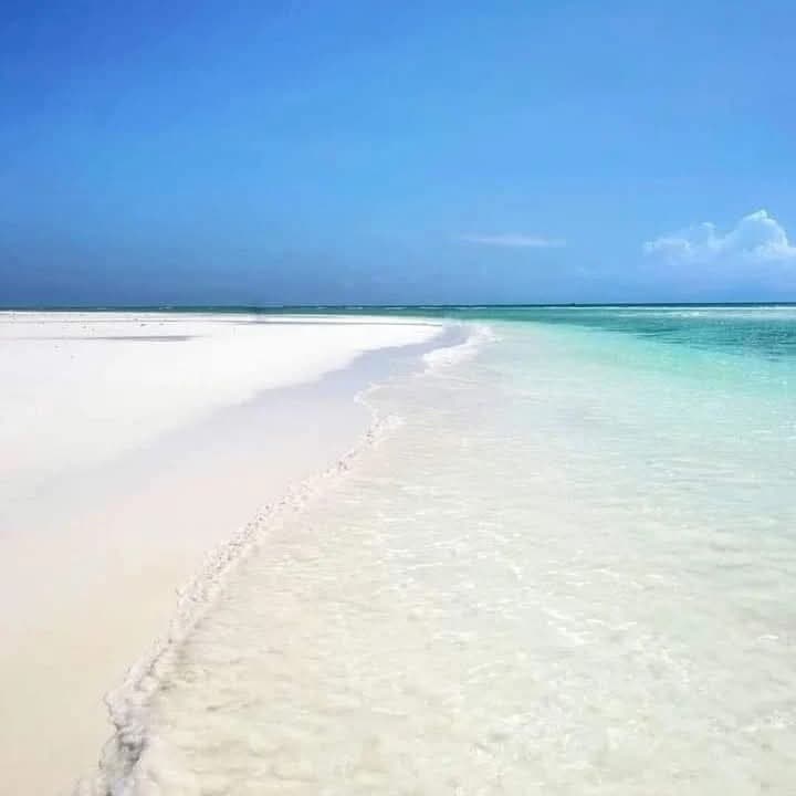 A white sandbank curving into turquoise water under a blue sky