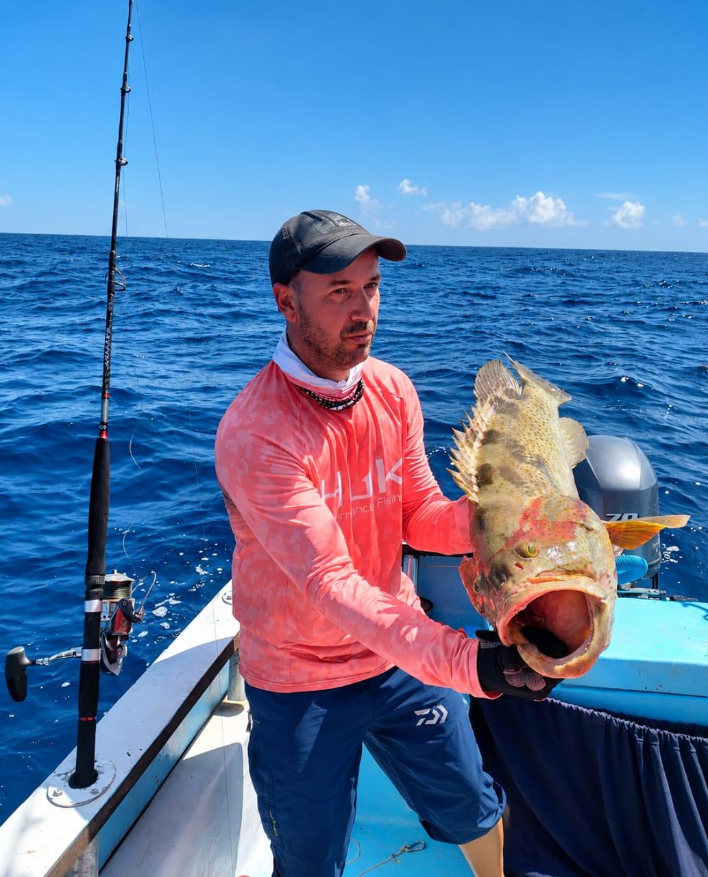 An angler at the rail holding up a mottled grouper