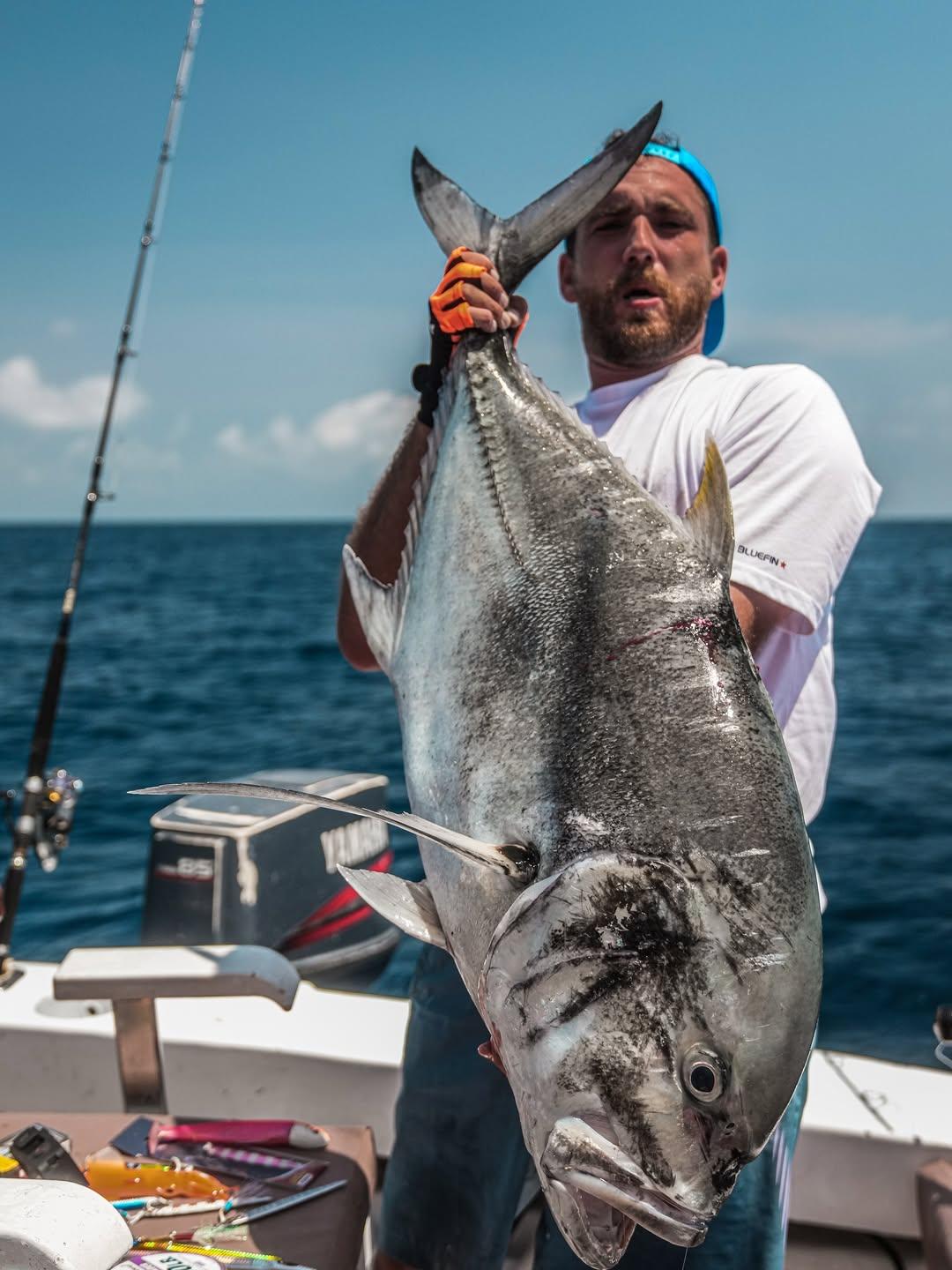 An angler holding a giant trevally up by the tail on a sunny day at sea
