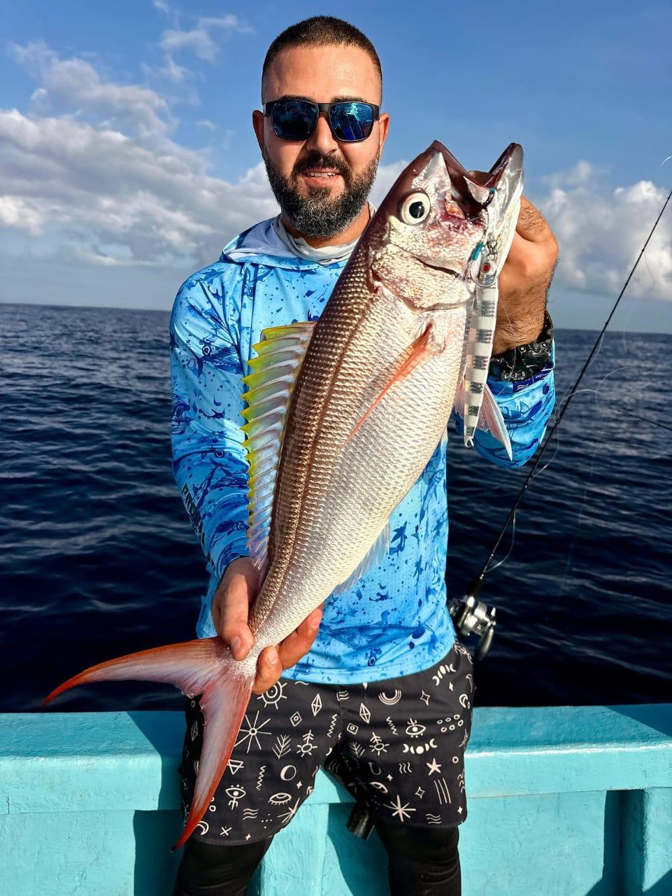 An angler holding up a long red snapper with the sea behind him