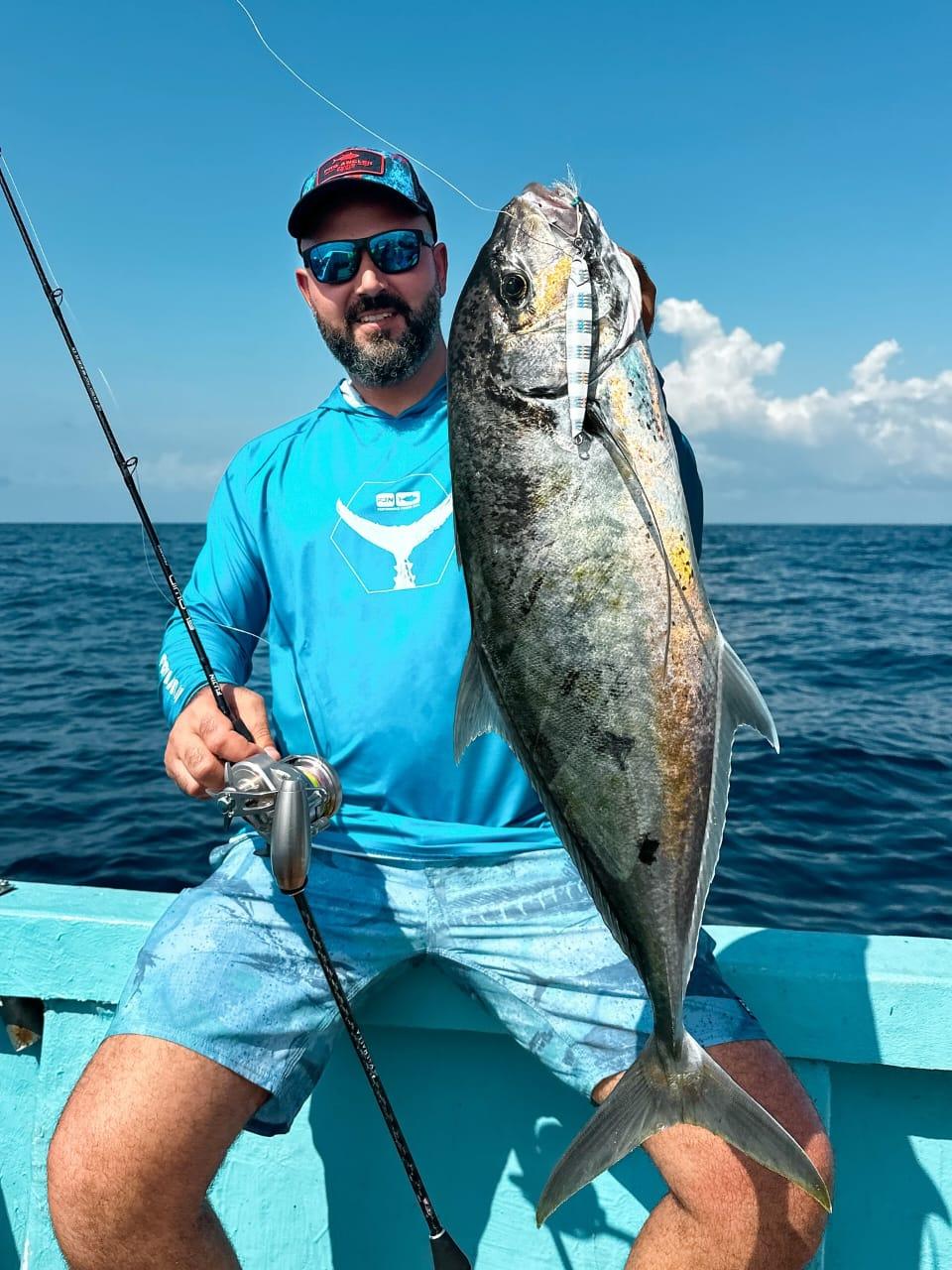 An angler holding a trevally beside his jigging rod