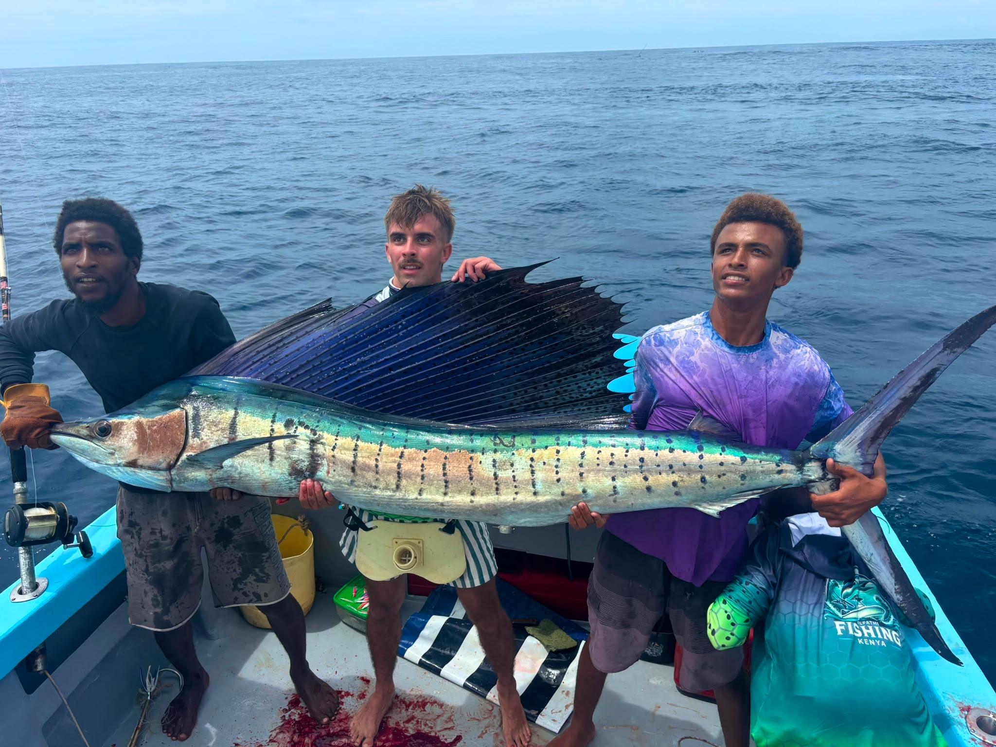3 crew holding up a sailfish with its sail spread on the deck