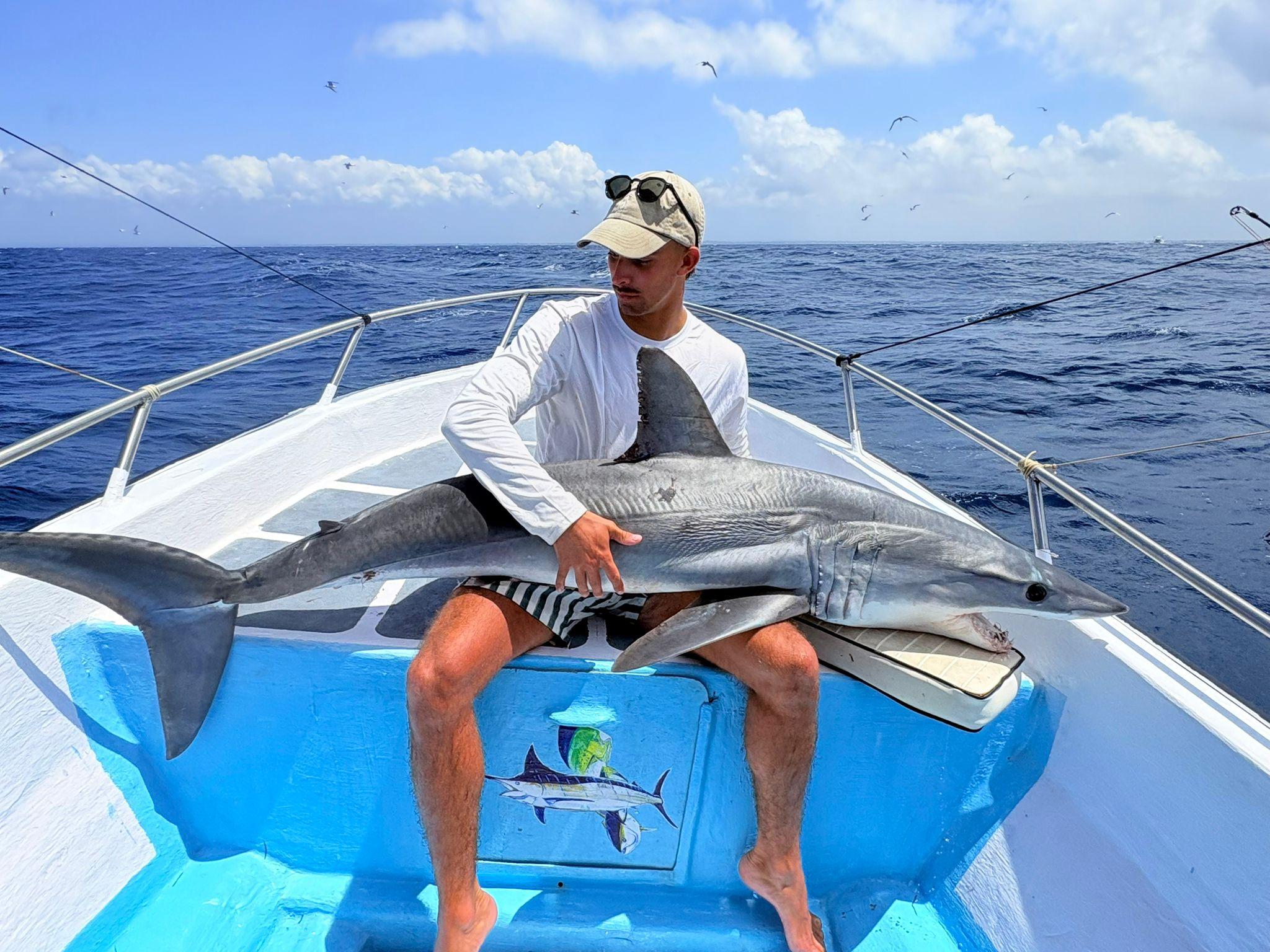 An angler sitting in the bow holding a shark across his lap