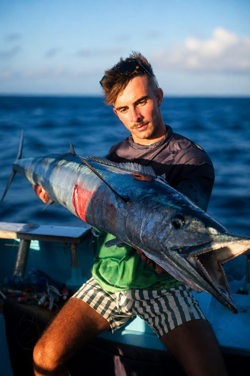 An angler holding a wahoo at the stern in evening light