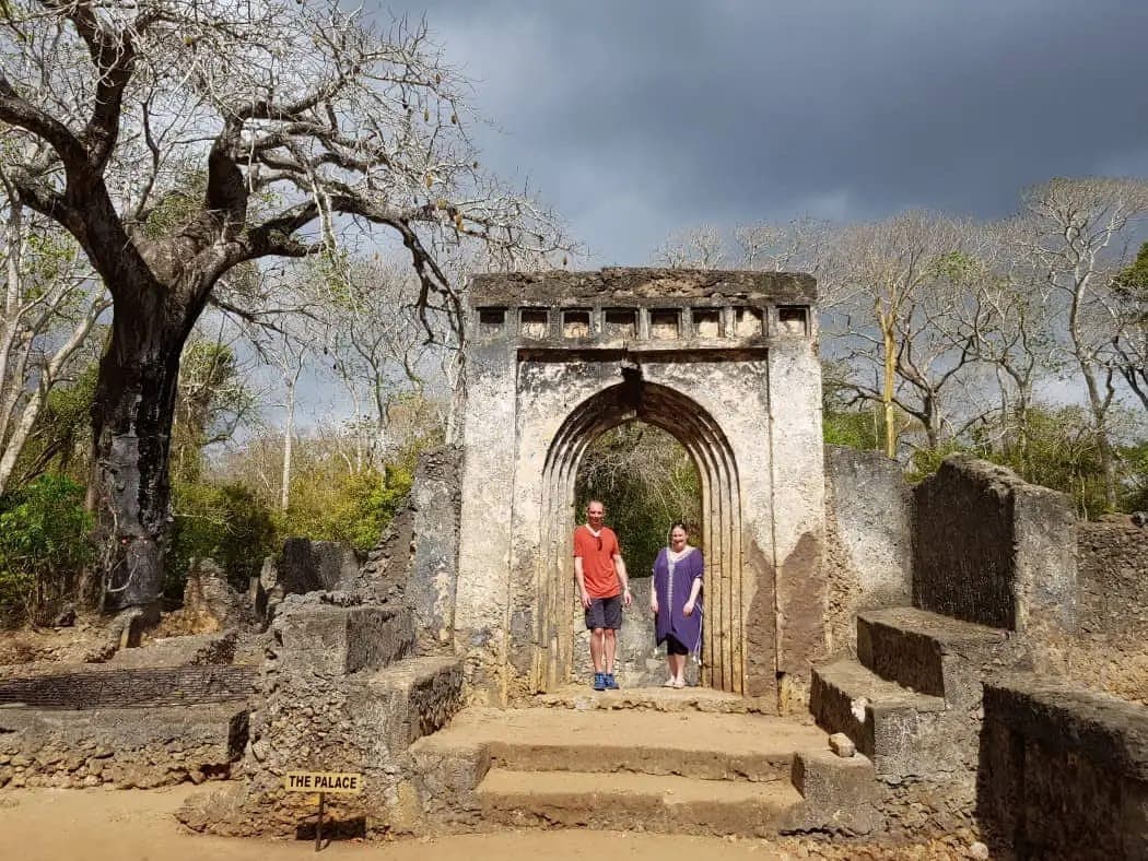 2 visitors standing in the stone arch of the palace at the Gede ruins