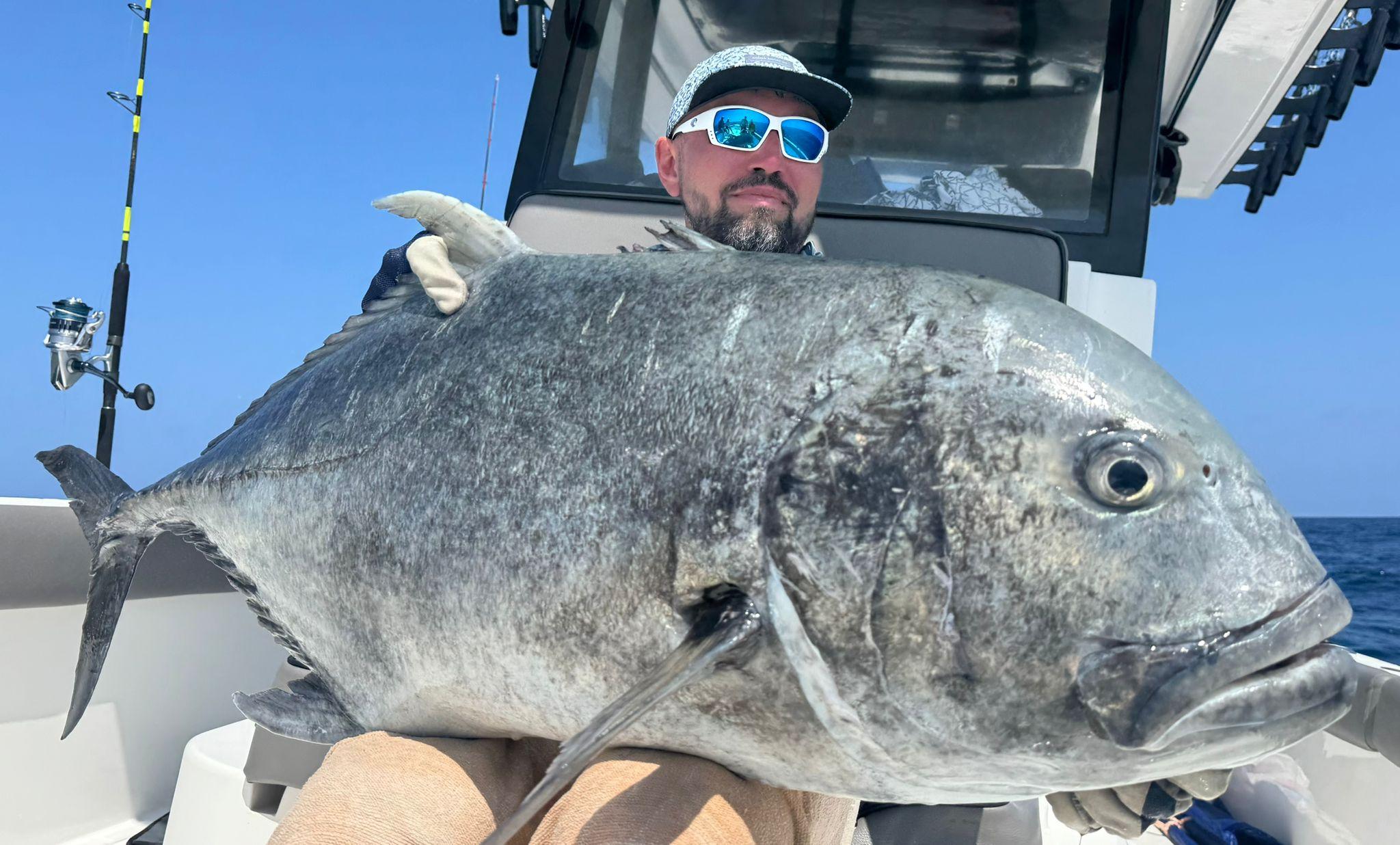 An angler holding a big giant trevally across his knees in the cockpit