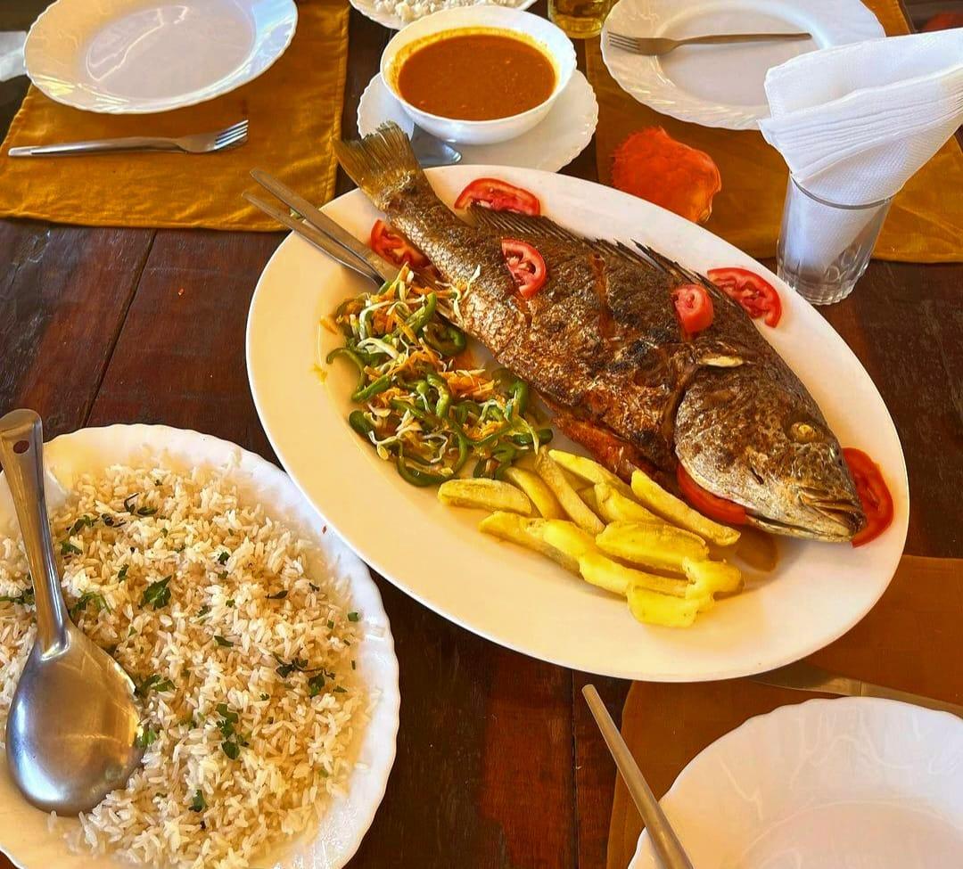 A seafood lunch of whole grilled fish with chips, coconut rice and sauce on a wooden table